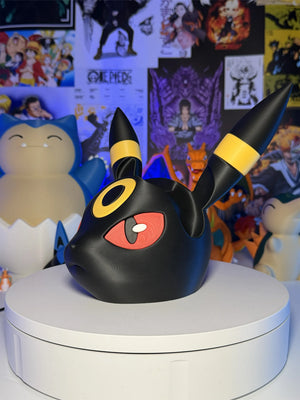 Testa di Umbreon Pokémon in resina su base bianca, sfondo con poster anime e figure.