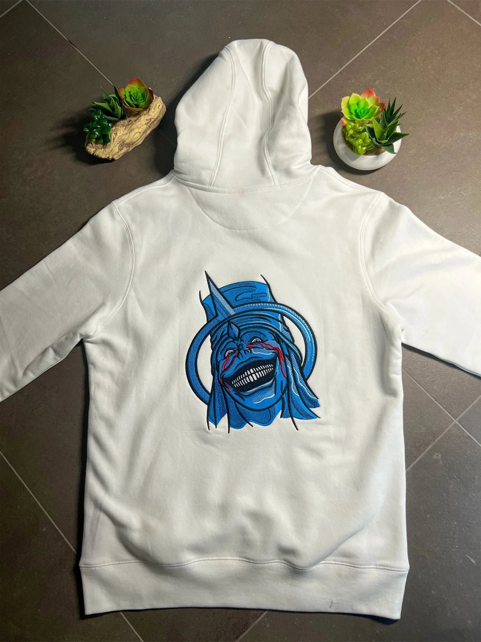Felpa bianca ricamata con statua manga blu ispirata a Solo Leveling, su sfondo scuro