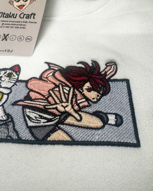 Felpa bianca con ricamo anime Dandadan, personaggio femminile in posa dinamica.