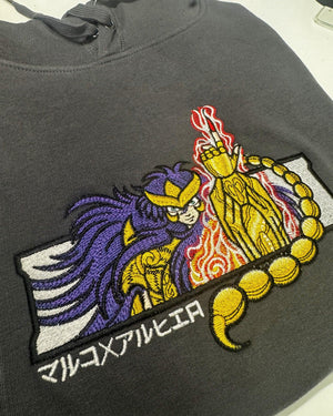 Felpa nera con ricamo anime, personaggio oro e viola ispirato a Saint Seiya, dettaglio scorpione.