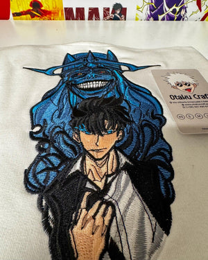 Felpa bianca ricamata con personaggio anime di Solo Leveling, dettaglio colorato in primo piano.