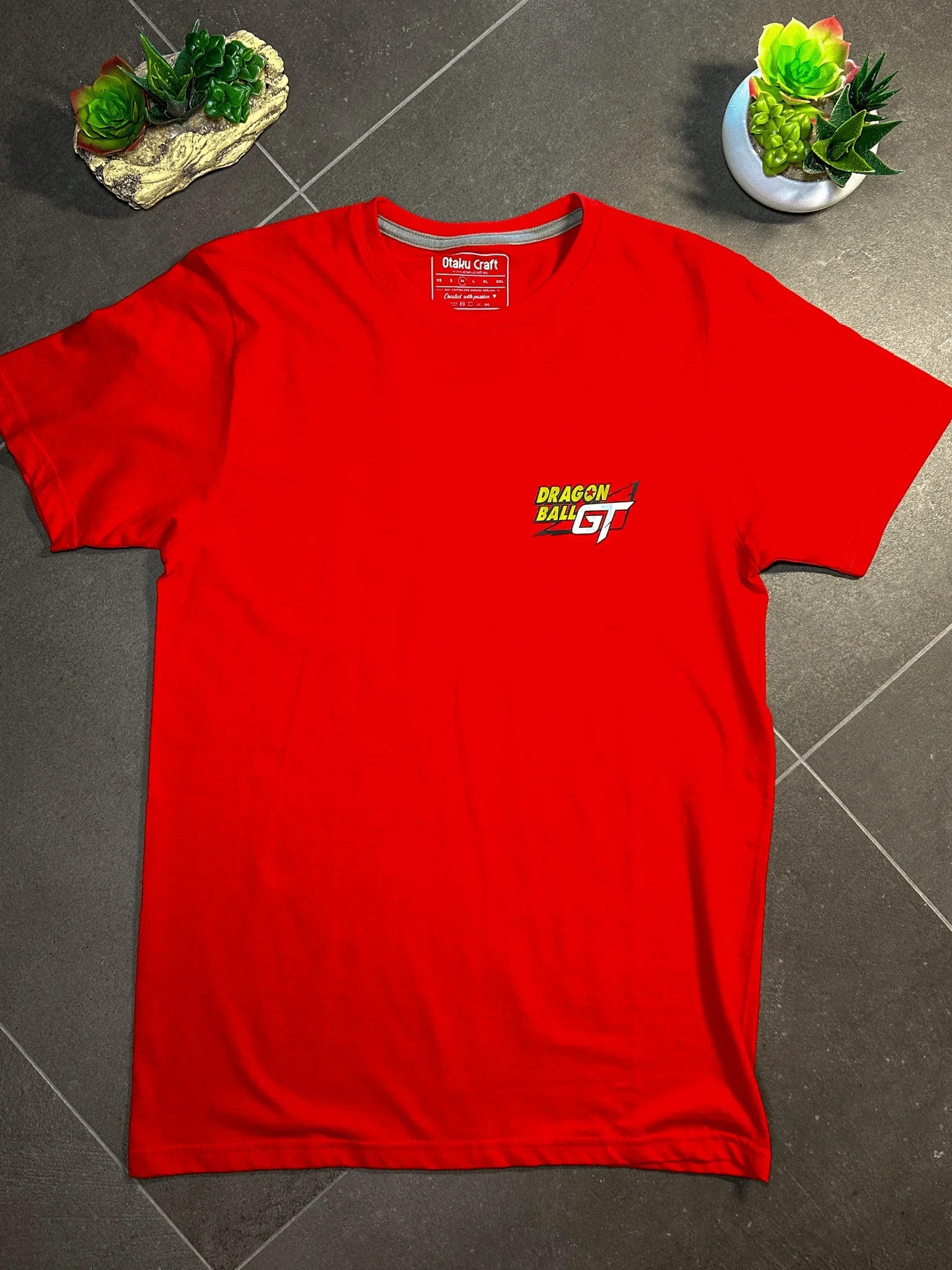 Maglietta rossa Dragon Ball GT con logo stampato sul petto, su sfondo grigio.
