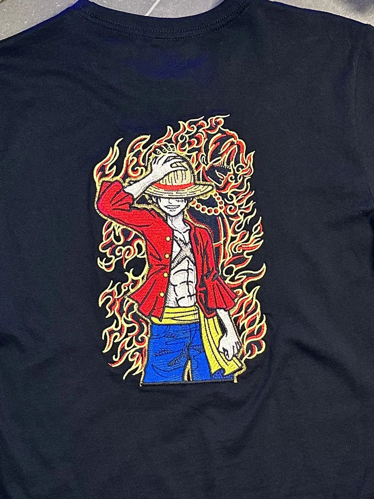 Maglietta nera ricamata con personaggio anime One Piece, Luffy tra fiamme rosse e gialle.