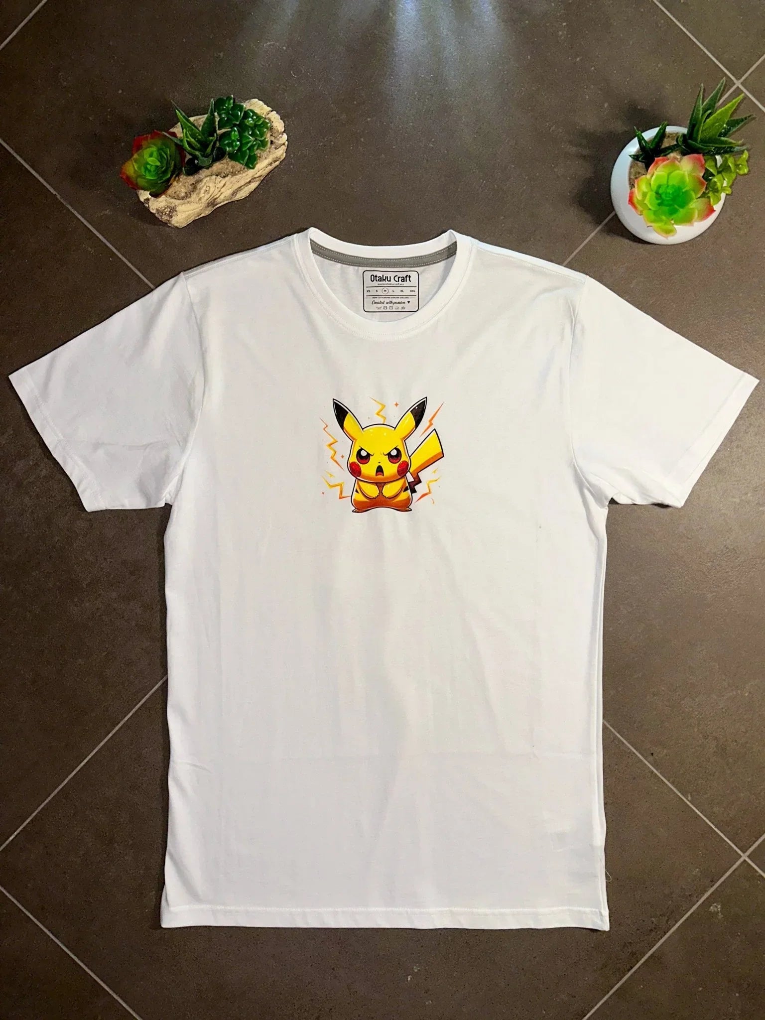 Maglietta bianca con stampa di Pikachu fulmine, stile anime, su sfondo marrone con piante.