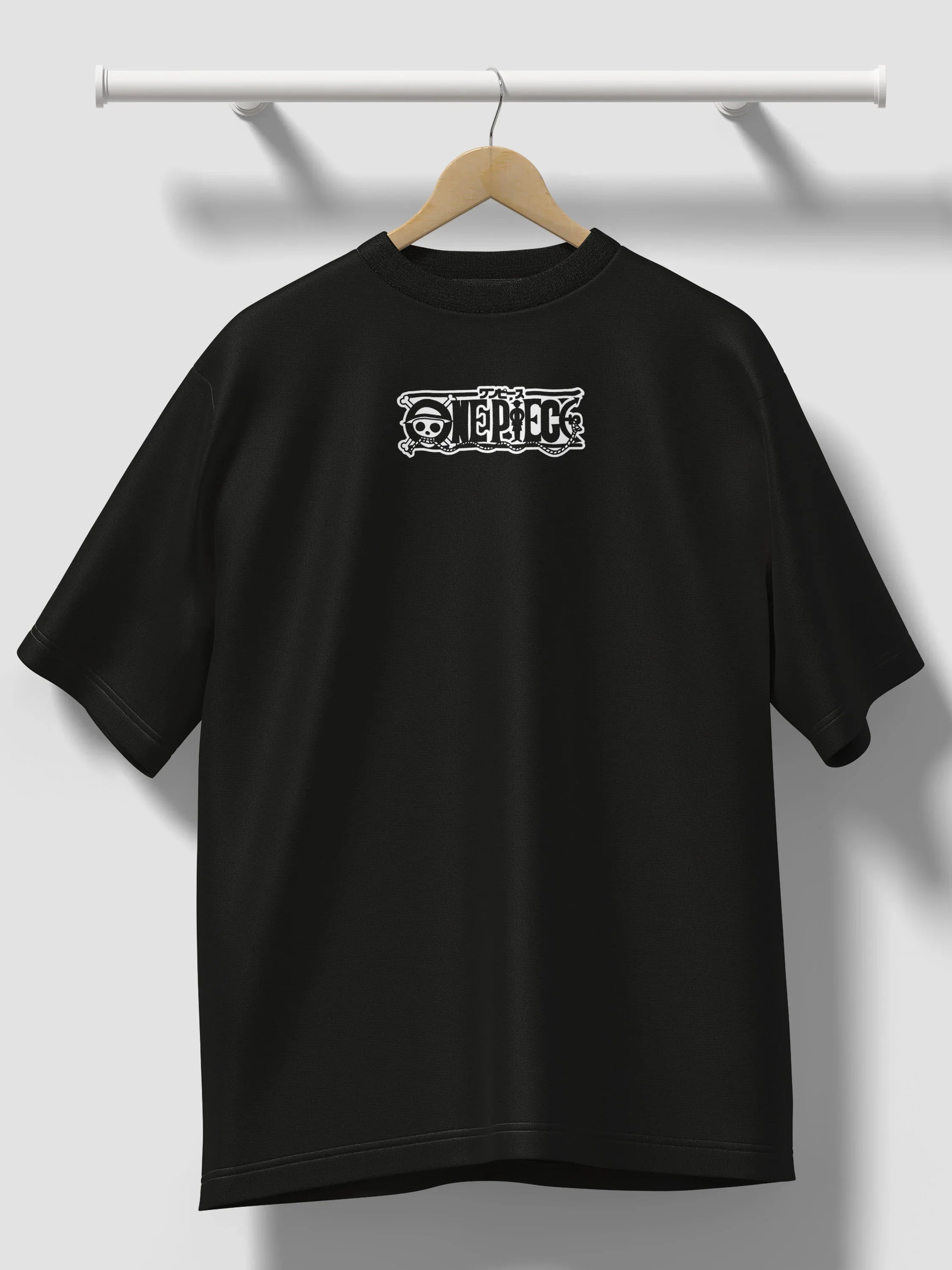 T-shirt oversize nera con logo One Piece ricamato, appesa a una gruccia contro parete chiara.