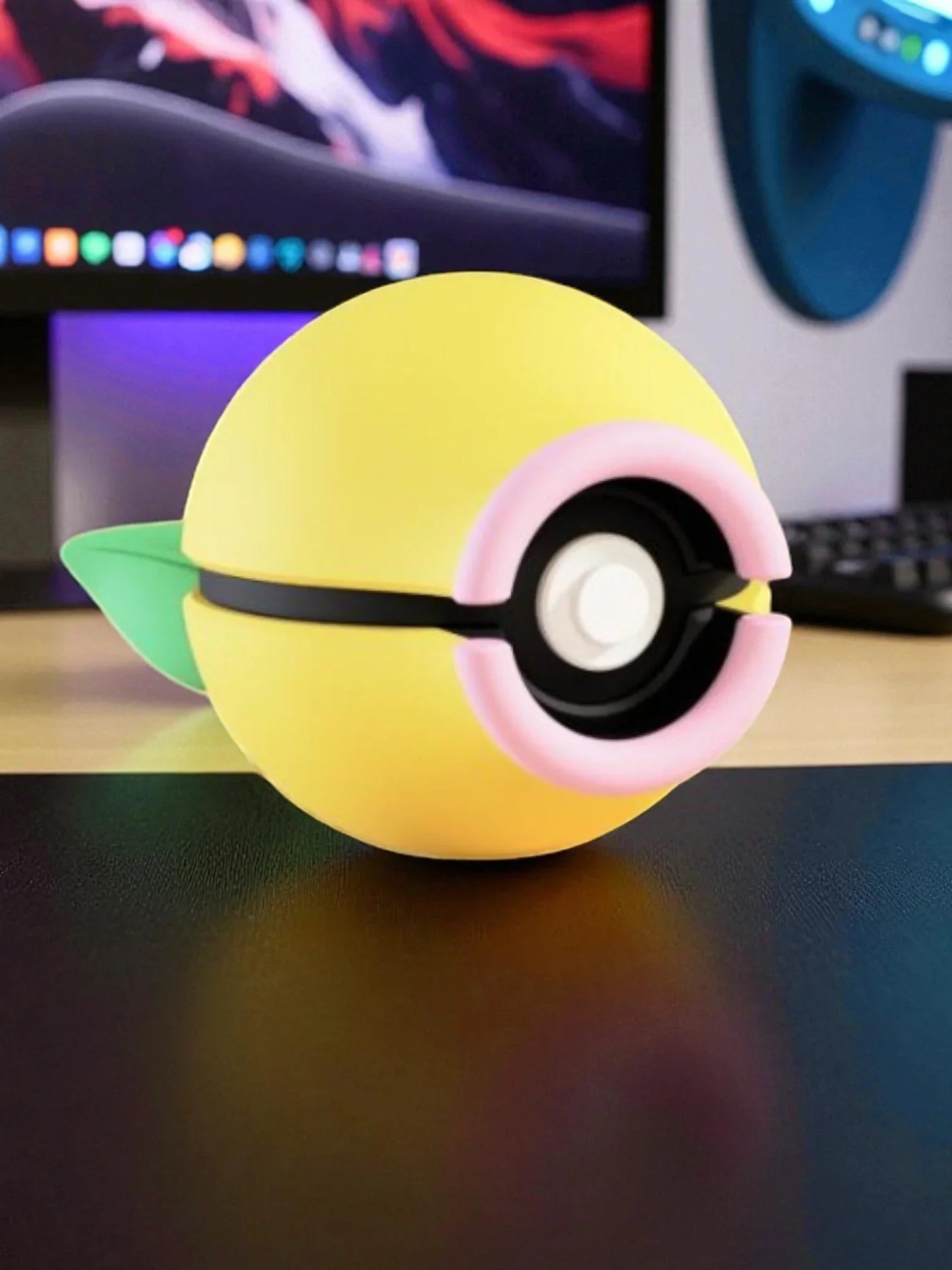 Pokeball gialla con dettagli rosa e foglia verde su scrivania, accessorio collezione anime