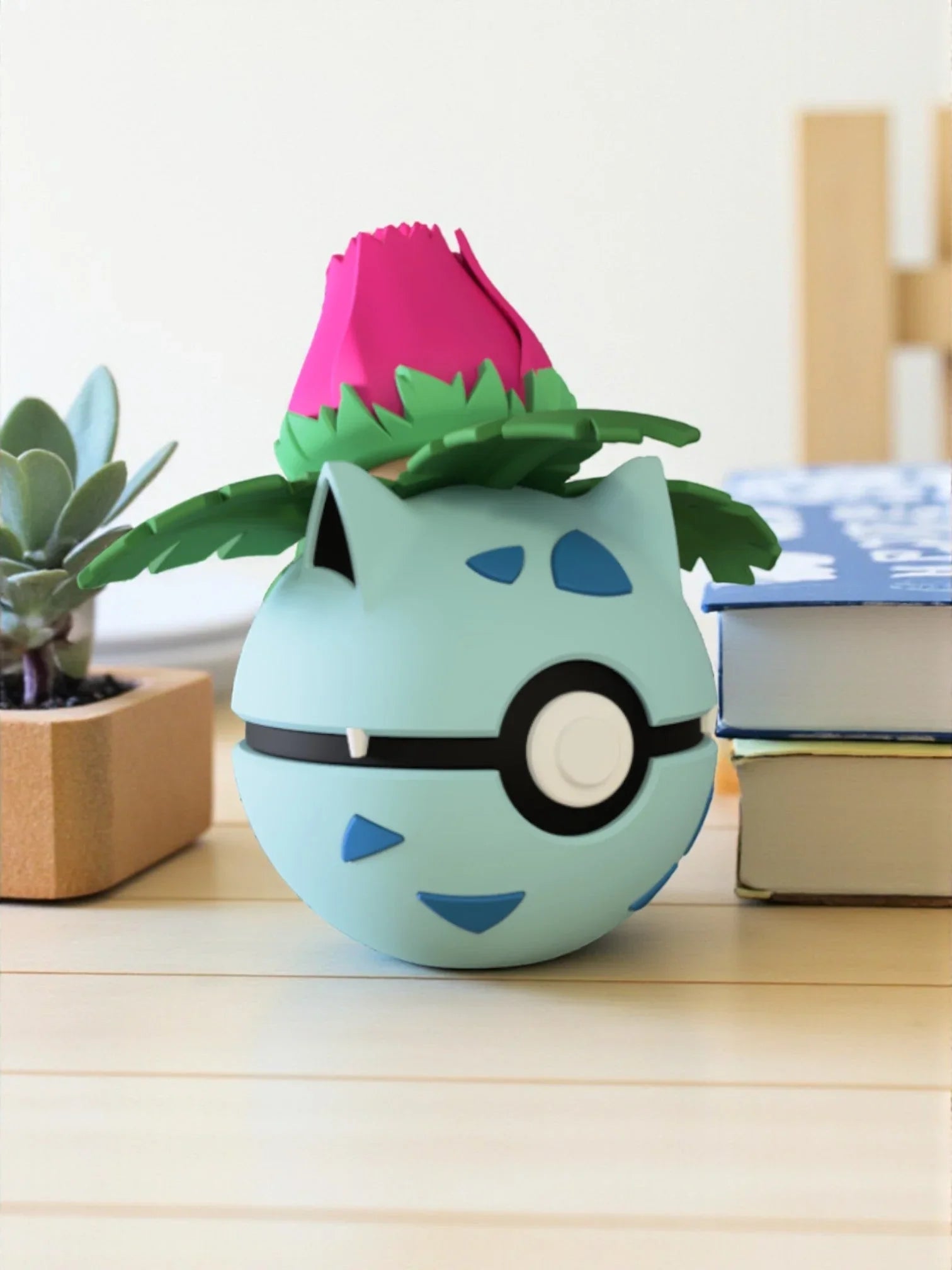 Pokeball decorativa ispirata a Ivysaur con base magnetica, su tavolo accanto a libri e pianta.