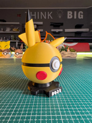 Pokeball ispirata a Pikachu in plastica 3D, con base magnetica numerata #025, su tavolo da lavoro.