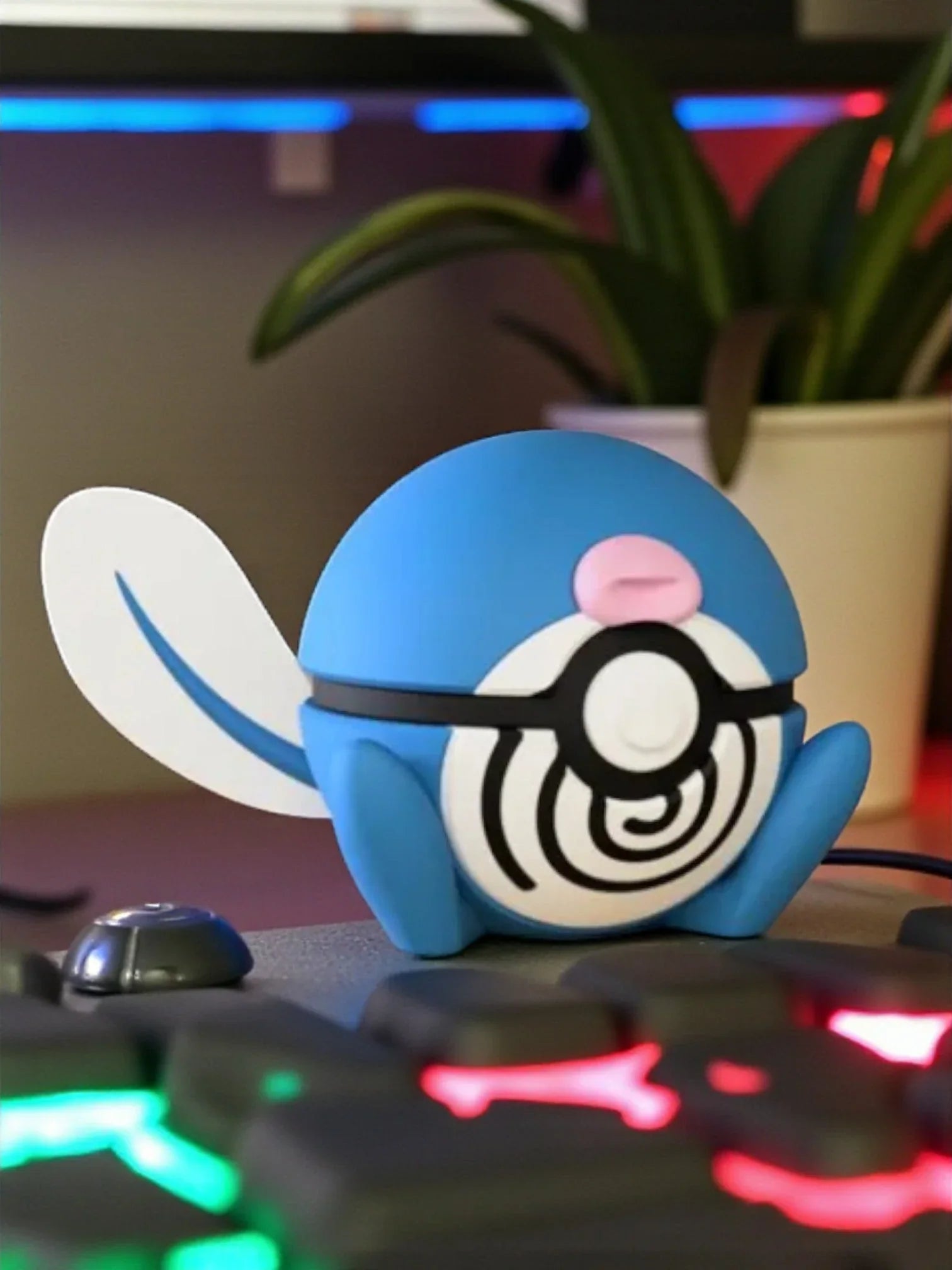 Figura Poliwag Pokémon con base magnetica, dettagli blu, coda bianca, sfondo tastiera gaming.