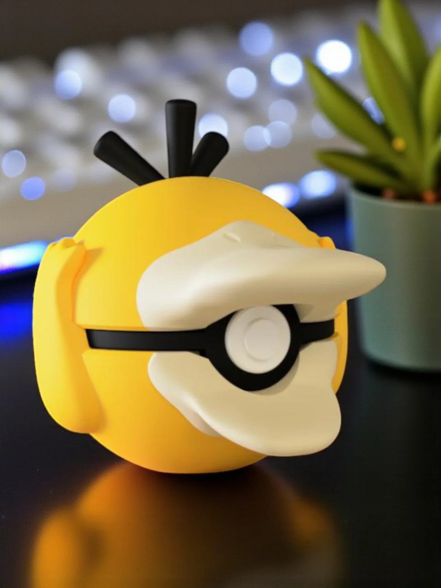 Pokeball Psyduck gialla con dettagli neri e bianchi, esposta su scrivania moderna
