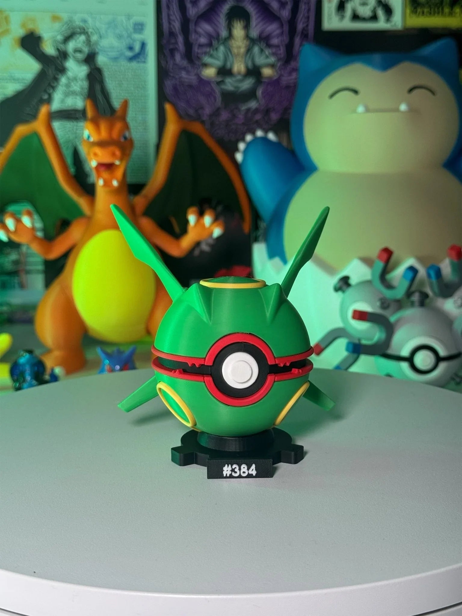 Pokeball ispirata a Rayquaza con base magnetica numerata, figure Pokémon sullo sfondo.