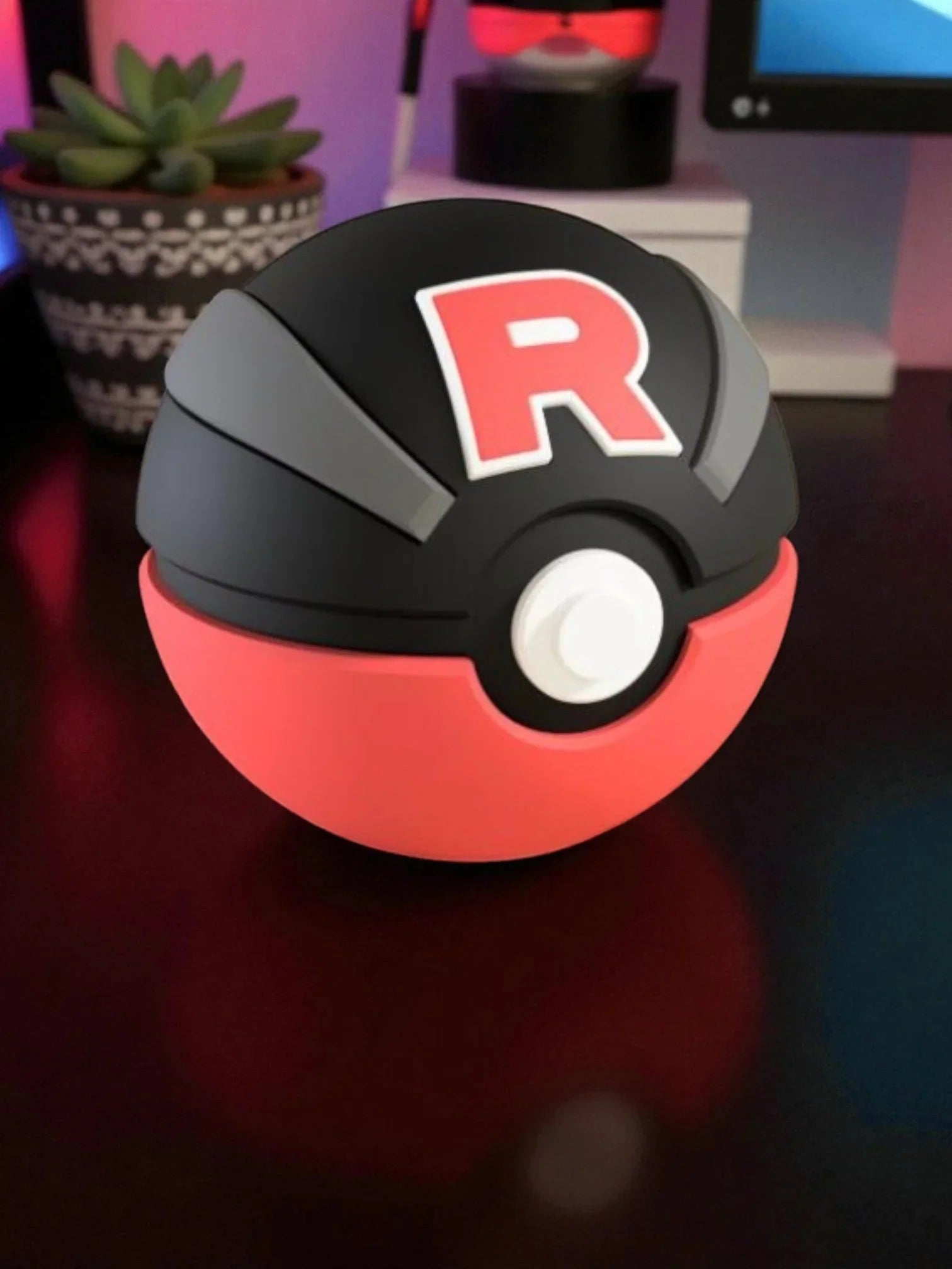Pokeball personalizzata Team Rocket nera e rossa con lettera R, su scrivania moderna.