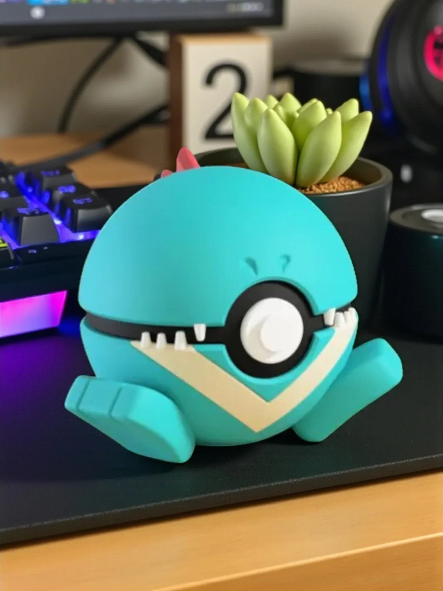 Figura Pokéball Totodile turchese con magnete, su scrivania accanto a tastiera e pianta