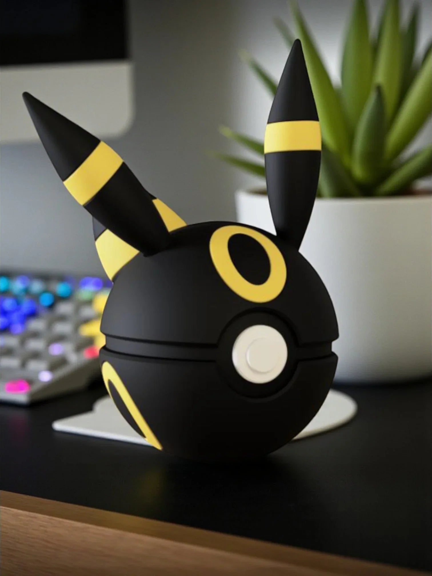 Pokeball Umbreon nera e gialla con orecchie, su scrivania moderna accanto a pianta