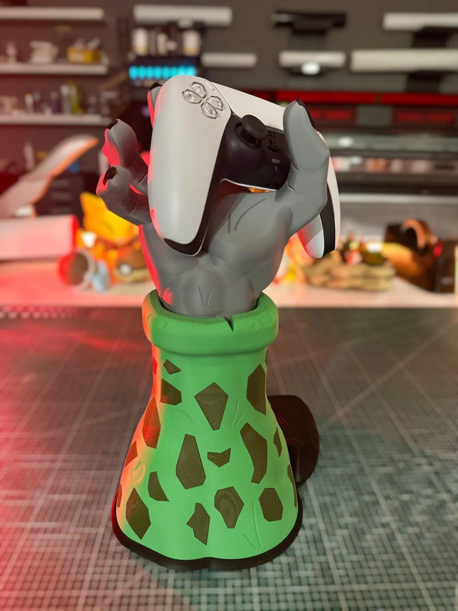 Supporto per controller ispirato a Dragon Ball Z, mano grigia con base verde decorata, regge un controller di gioco