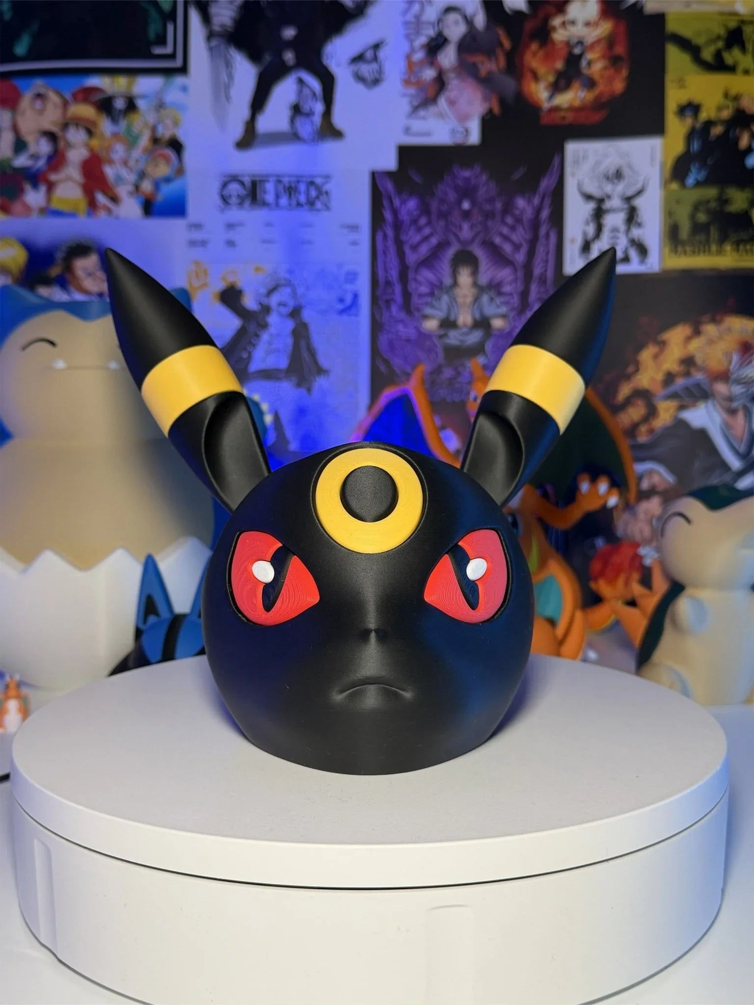 Supporto controller a forma di Umbreon Pokémon su base bianca, sfondo con poster anime.