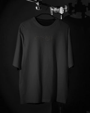 T-shirt nera ricamata Jujutsu Kaisen con scritta giapponese sul petto, fondo nero minimal.