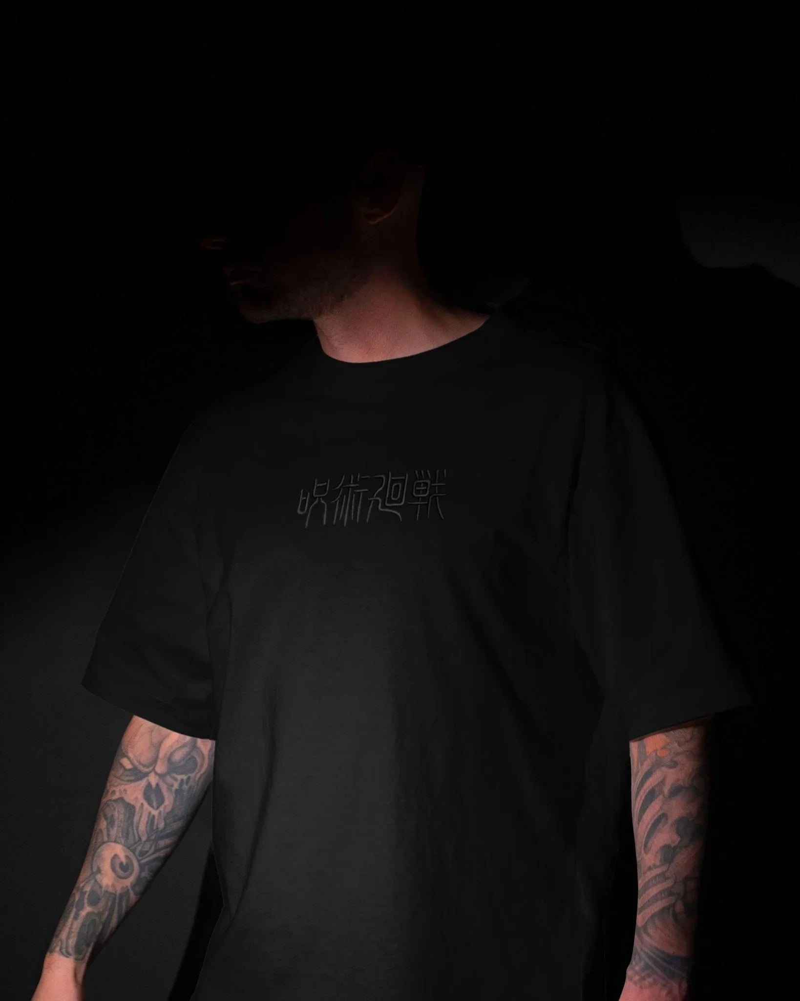 T-shirt nera Jujutsu Kaisen con scritta giapponese ricamata, indossata da uomo tatuato.