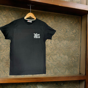 T-shirt nera One Piece con logo Mugiwara stampato sul petto, appesa su gruccia.