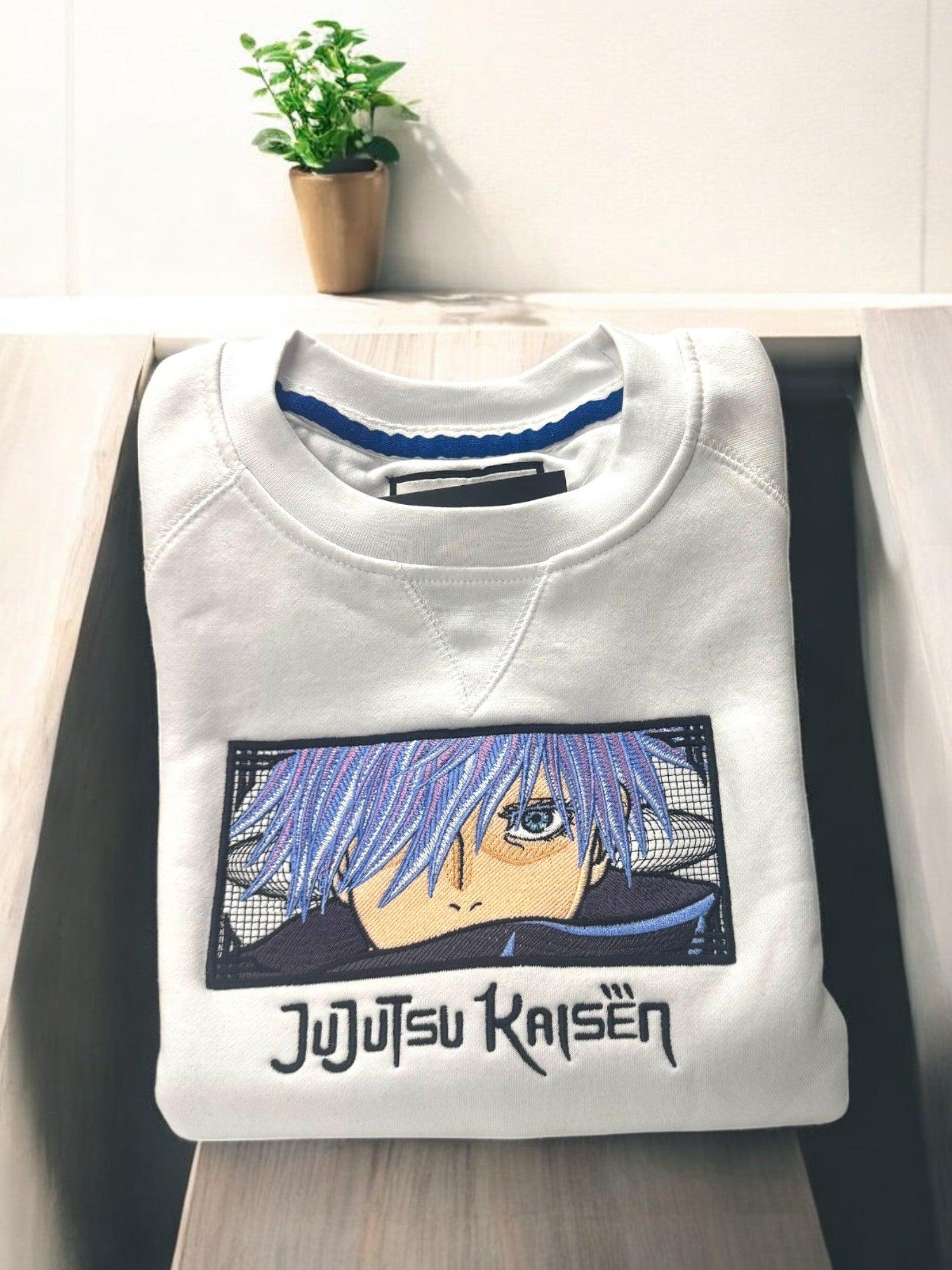 Felpa bianca ricamata con Gojo Satoru di Jujutsu Kaisen, piegata su una superficie chiara.