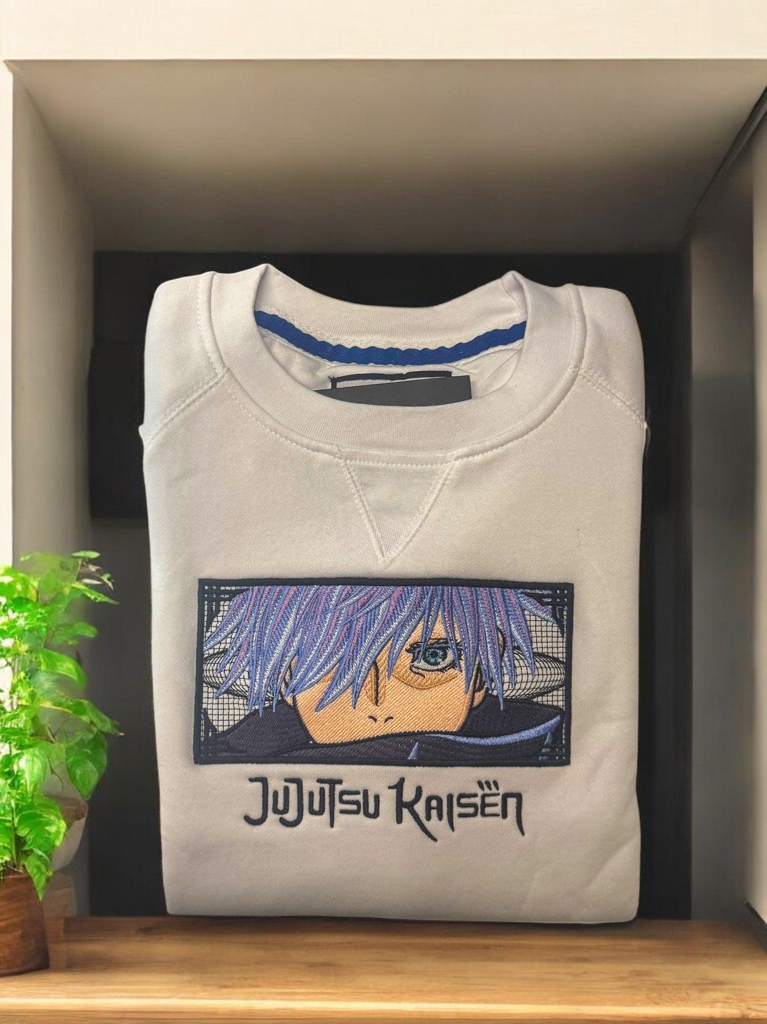 Felpa bianca ricamata con Gojo Satoru di Jujutsu Kaisen, piegata su scaffale.