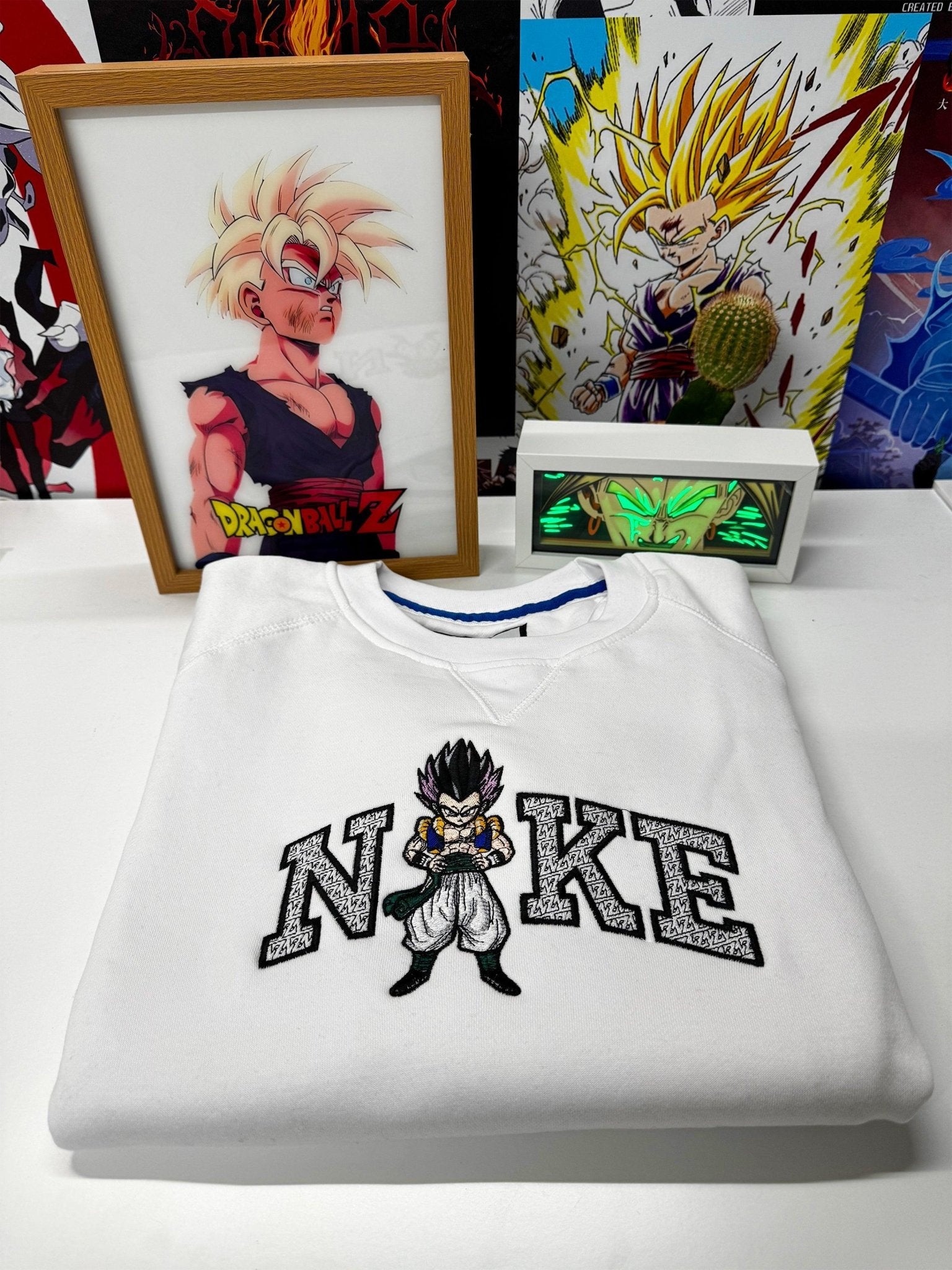 Felpa bianca ricamata con personaggio anime ispirato a Dragon Ball e scritta stilizzata, esposta su sfondo con stampe e illustrazioni anime.