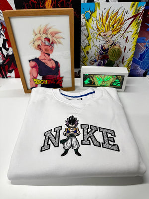 Felpa bianca ricamata con personaggio anime ispirato a Dragon Ball e scritta stilizzata, esposta su sfondo con stampe e illustrazioni anime.