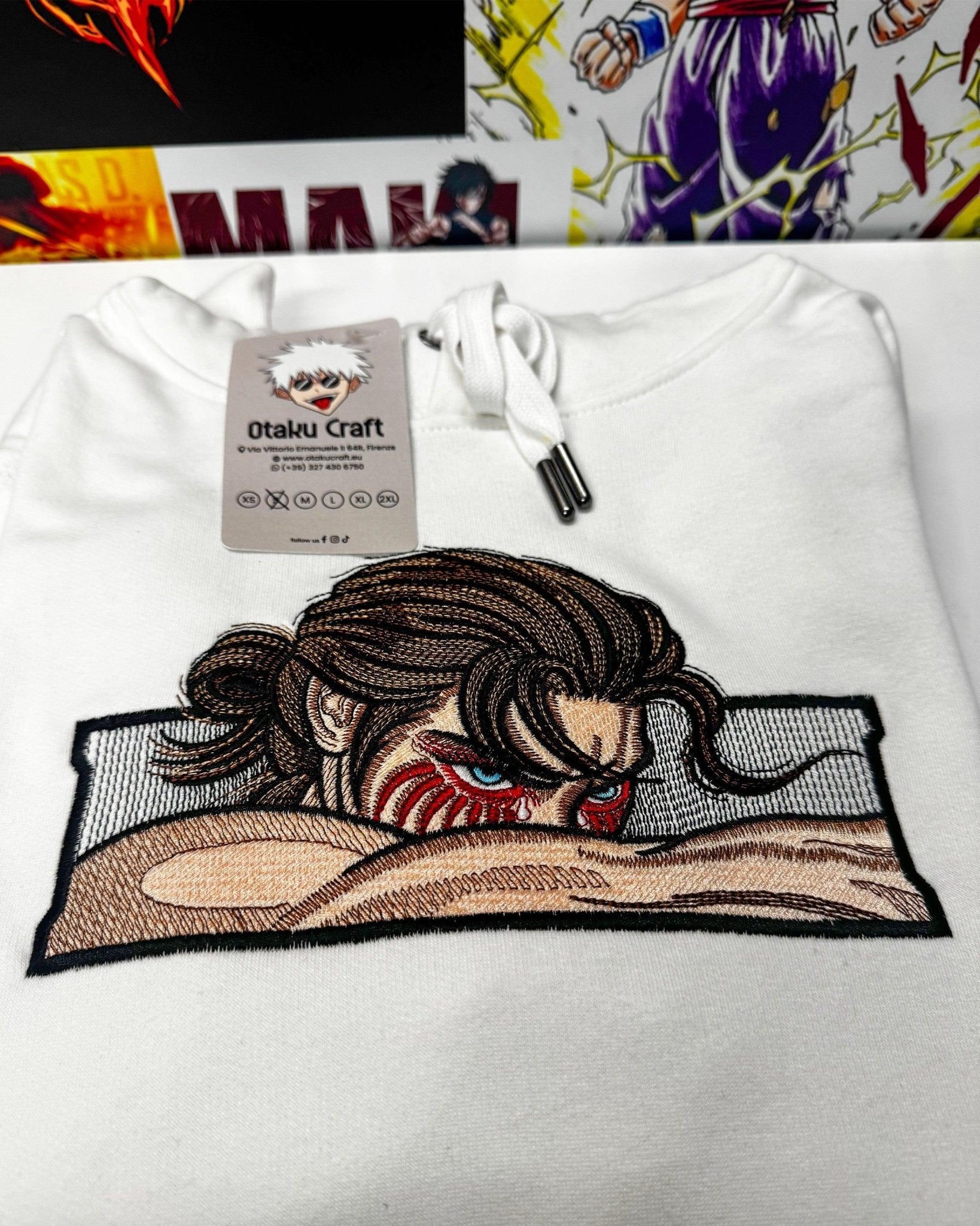Felpa bianca anime con ricamo di personaggio ispirato a Attack on Titan, sfondo manga colorato.