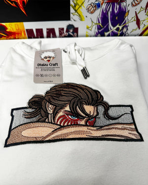 Felpa bianca anime con ricamo di personaggio ispirato a Attack on Titan, sfondo manga colorato.