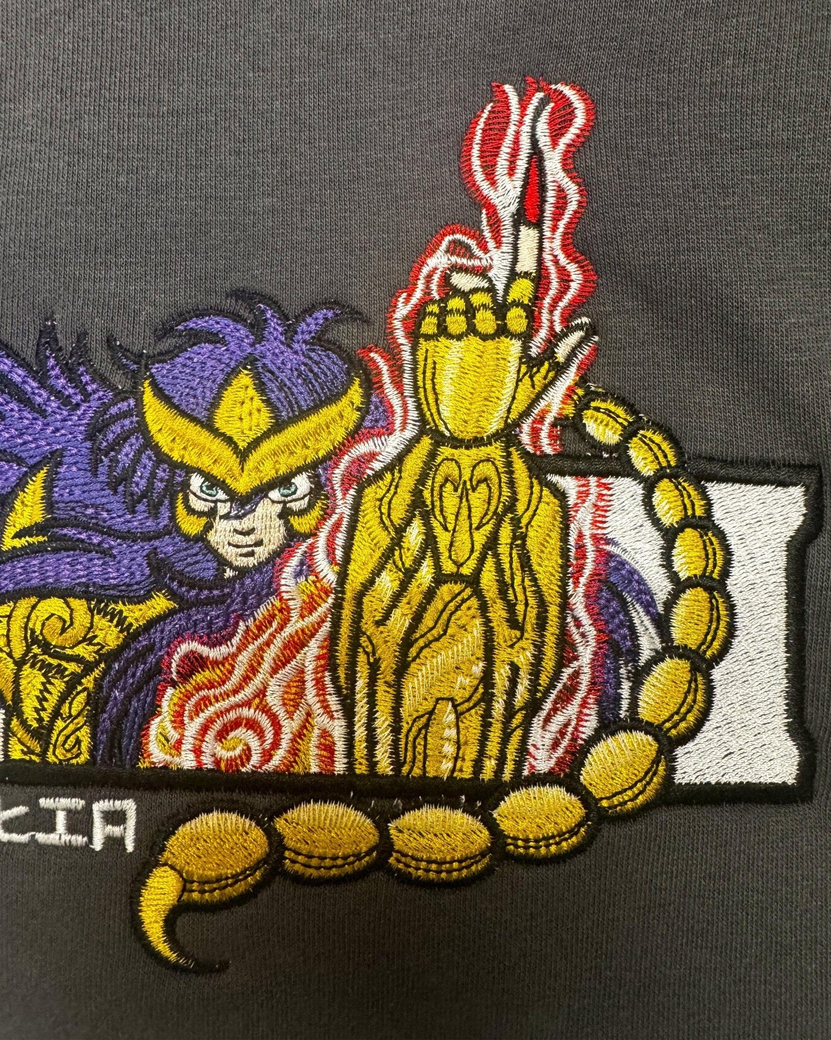 Ricamo anime di Milo dello Scorpione Saint Seiya su felpa grigia, fiammate rosse, dettagli oro