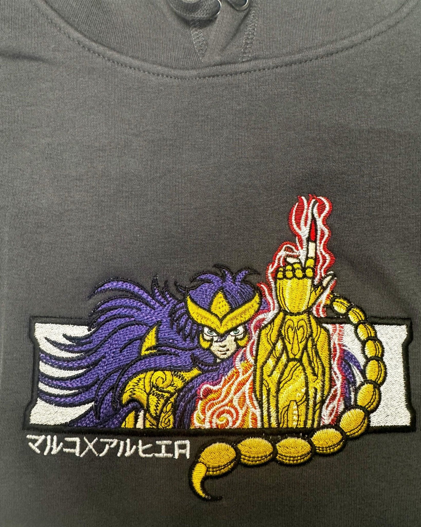 Felpa nera con ricamo anime, personaggio dorato ispirato a Saint Seiya e simbolo scorpione.