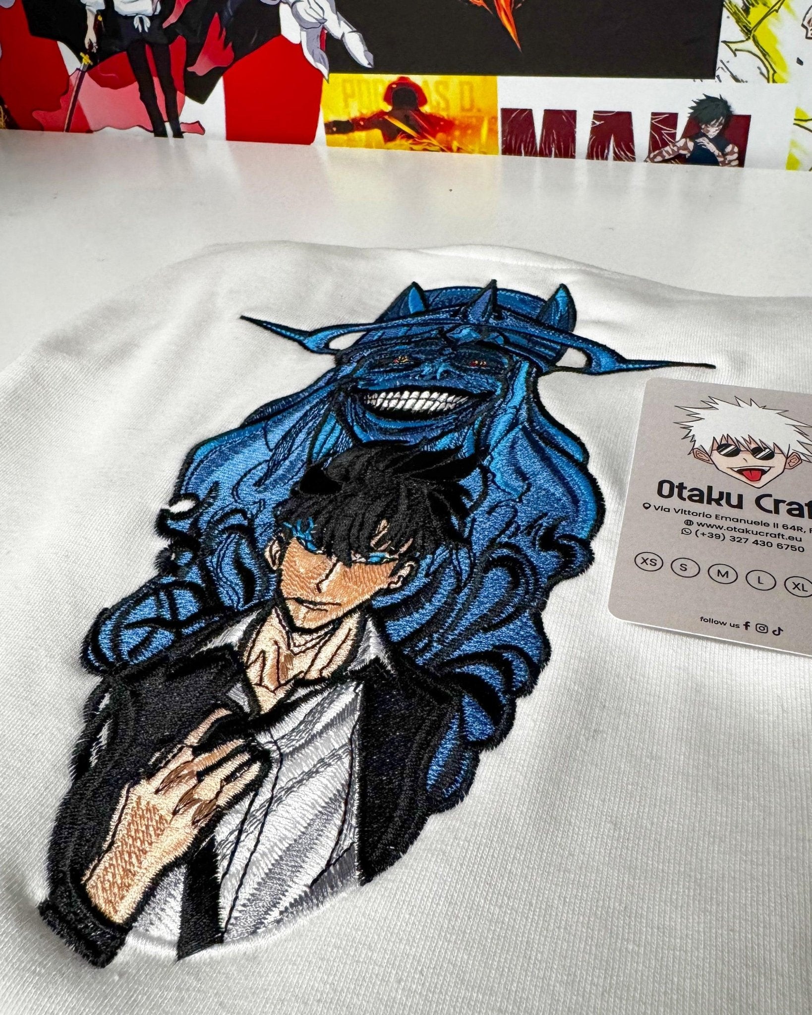 Felpa bianca con ricamo personaggio anime Solo Leveling, design dettagliato e colori vivaci.