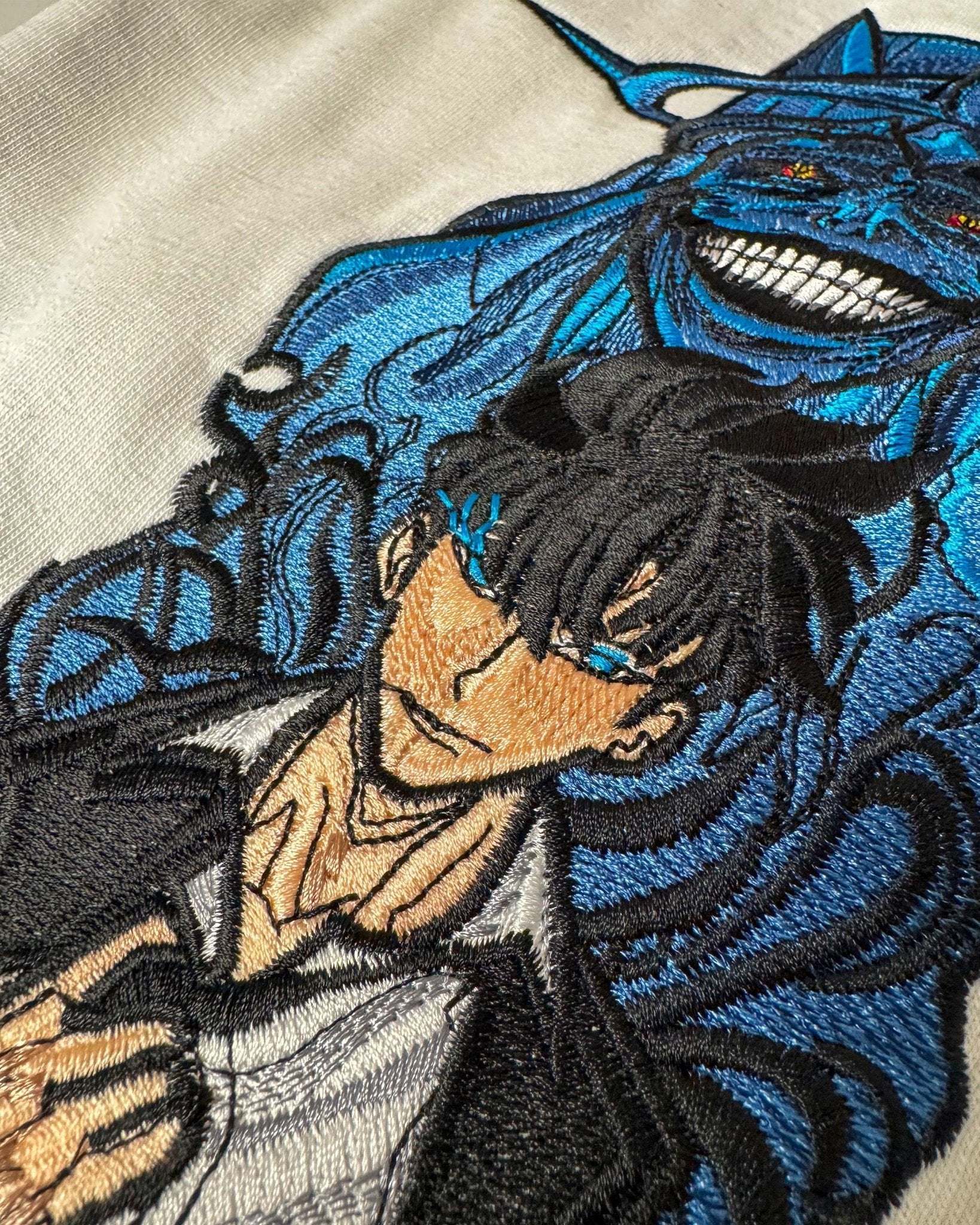 dettaglio ricamo anime su felpa, personaggio maschile con occhi azzurri e creatura blu sullo sfondo