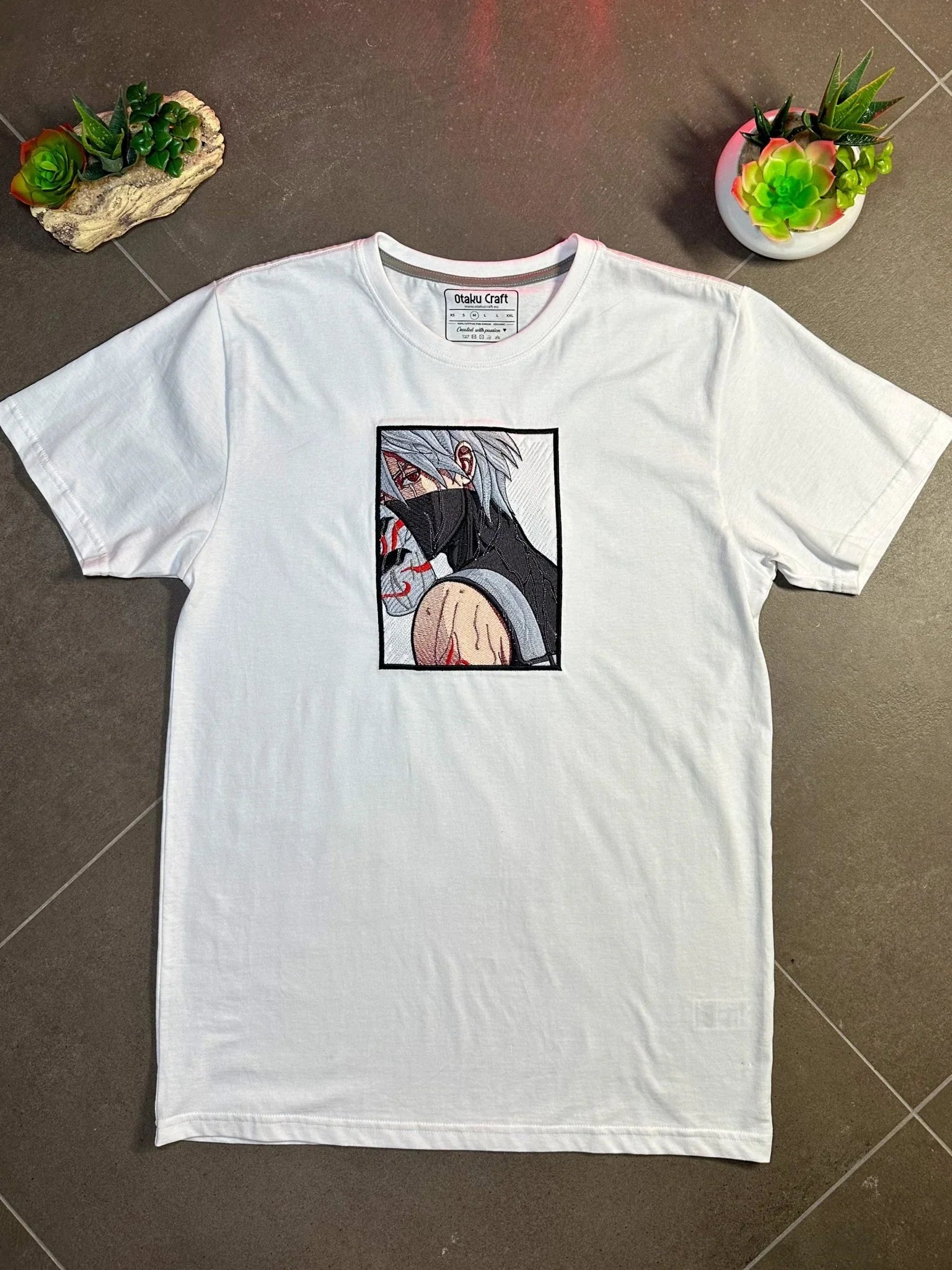 Maglietta bianca ricamata con personaggio anime dai capelli grigi e maschera nera, stile Kakashi Sharingan.