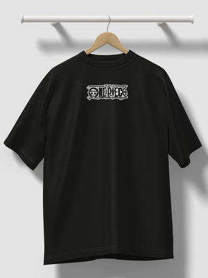 T-shirt oversize nera con logo One Piece ricamato, appesa a una gruccia contro parete chiara.