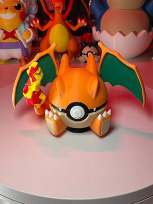Modellino Pokéball ispirato a Charizard con ali verdi, fiamma gialla e rossa, su tavolo.