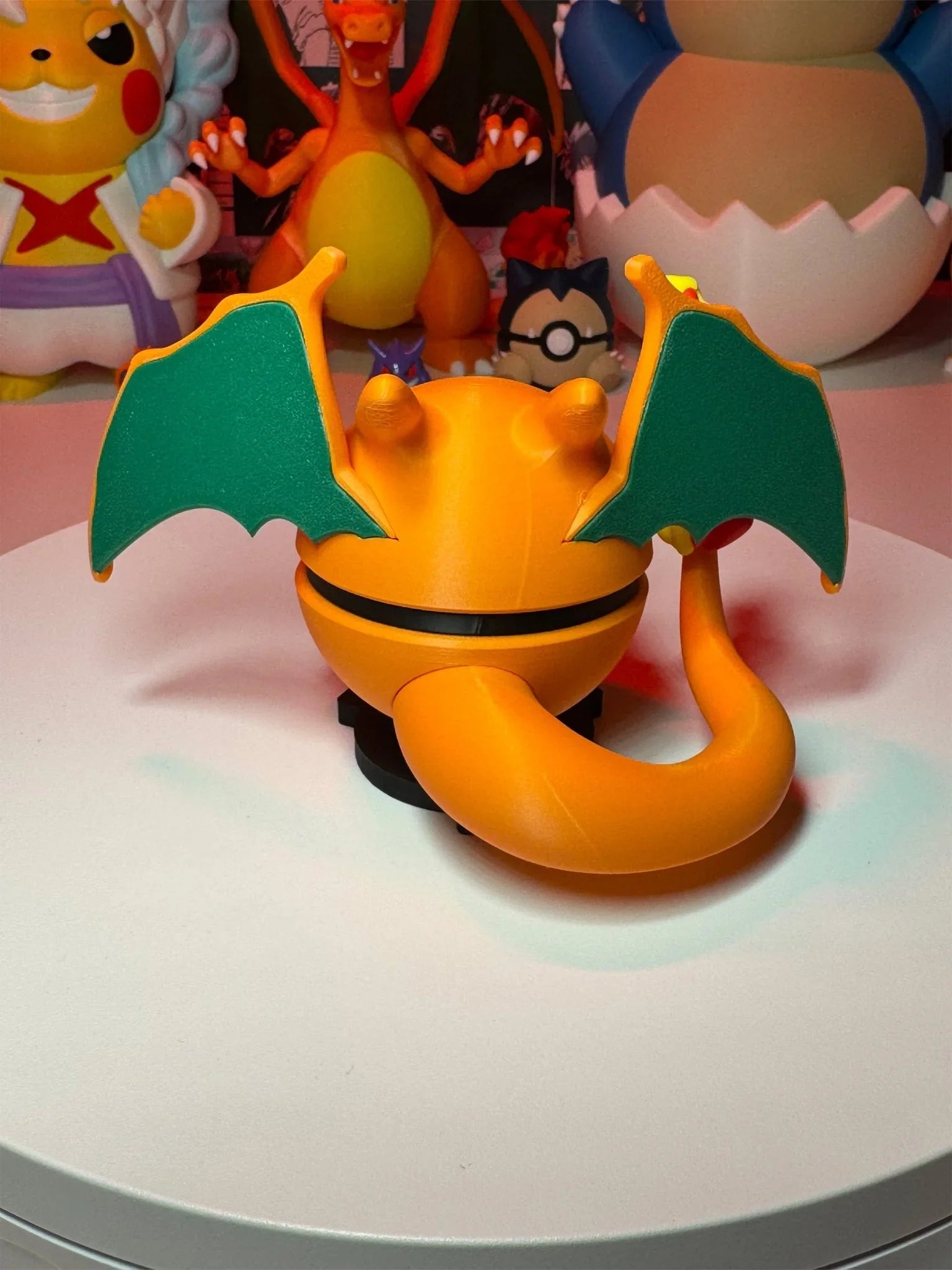 Pokeball ispirata a Charizard con ali, coda e figure anime Pokémon sullo sfondo.