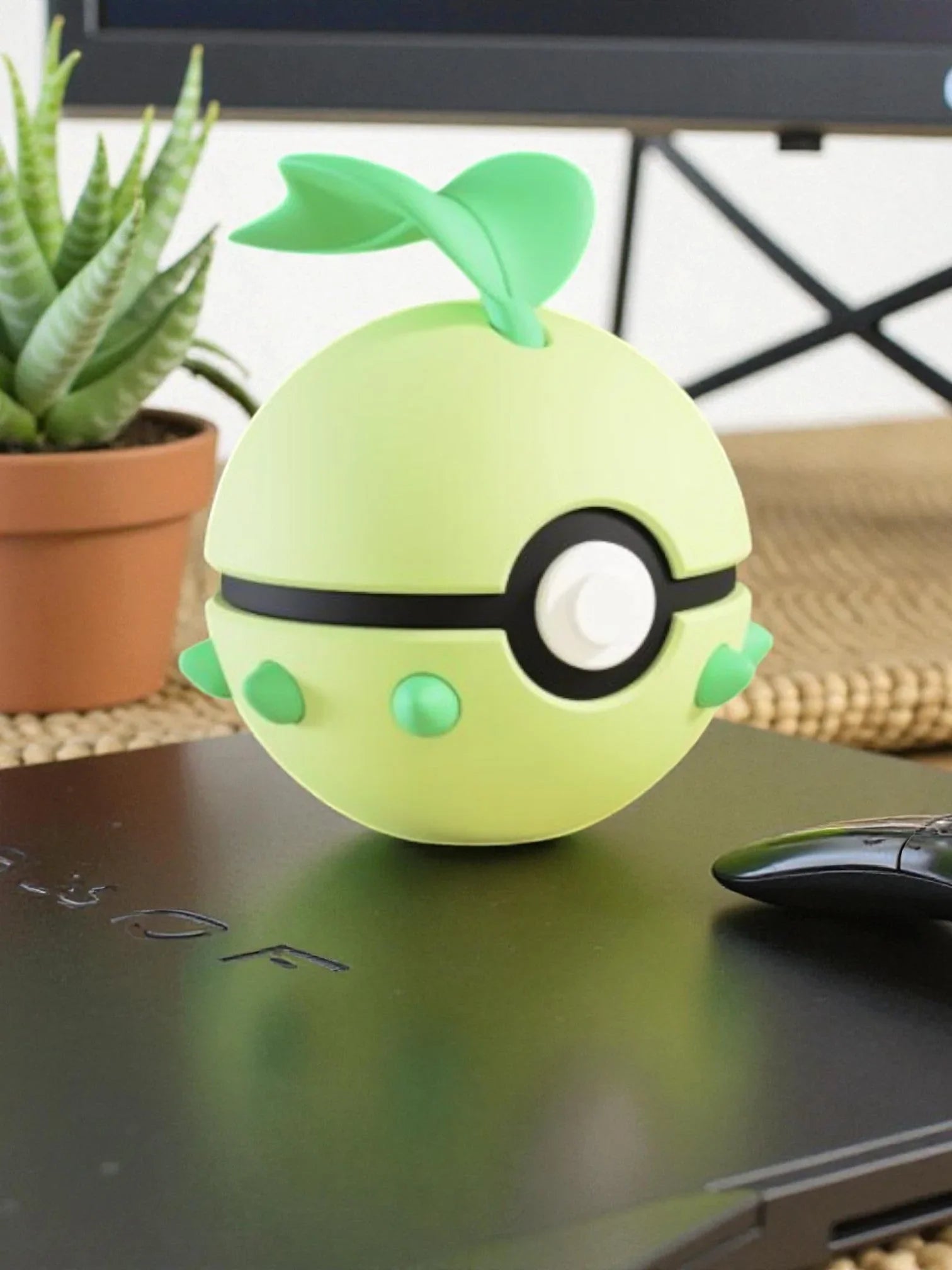 Pokeball ispirata a Chikorita verde con base magnetica, su scrivania accanto a pianta