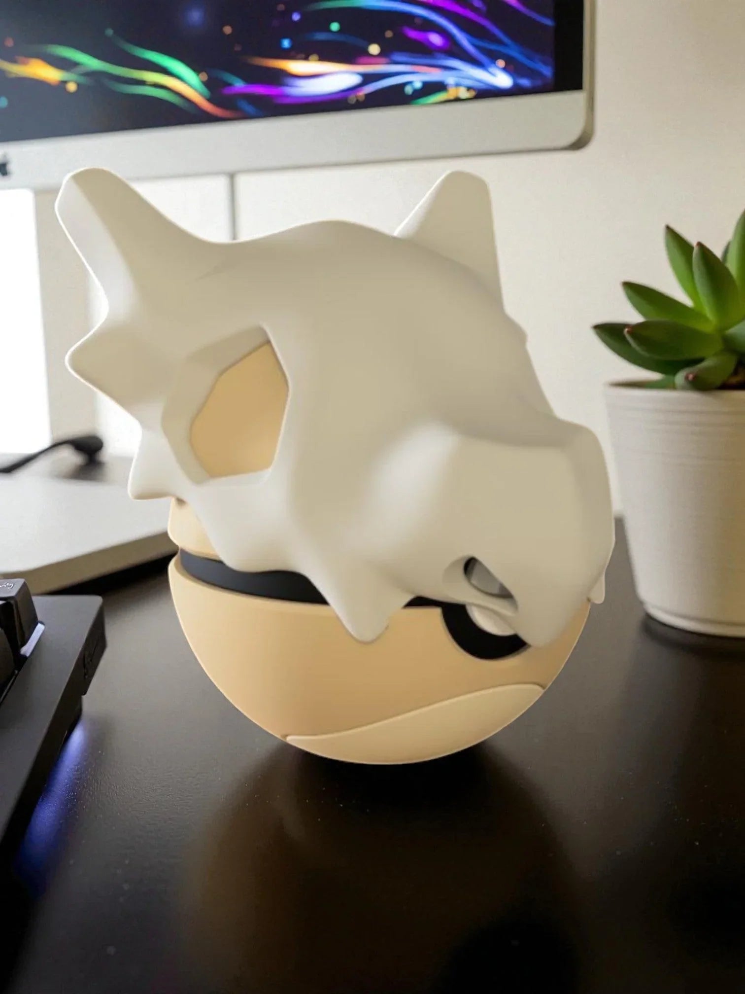 Pokeball decorativa ispirata a Cubone su scrivania accanto a pianta e computer