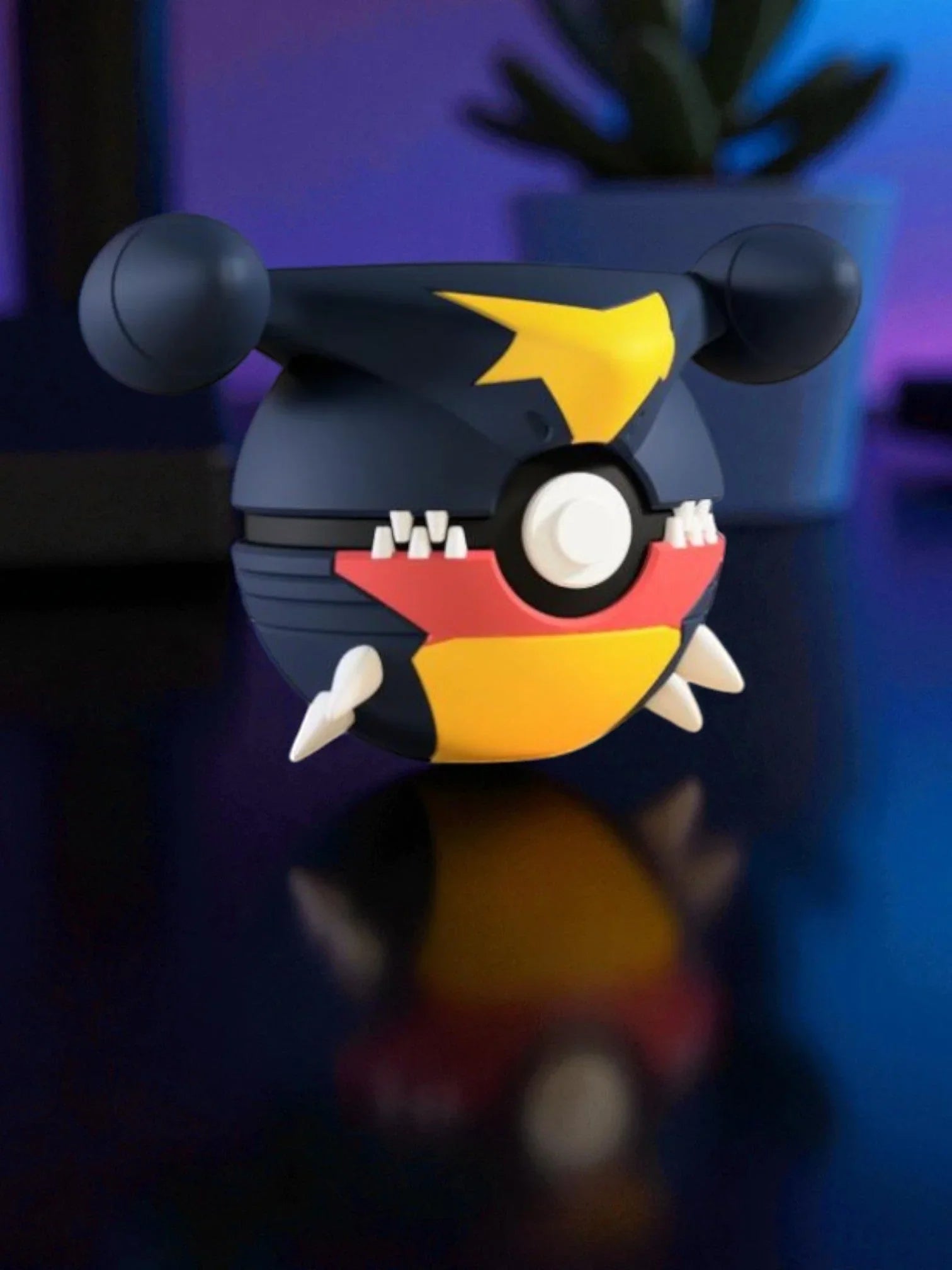 Pokeball ispirata a Garchomp, con dettagli colorati e base magnetica, su sfondo sfocato.