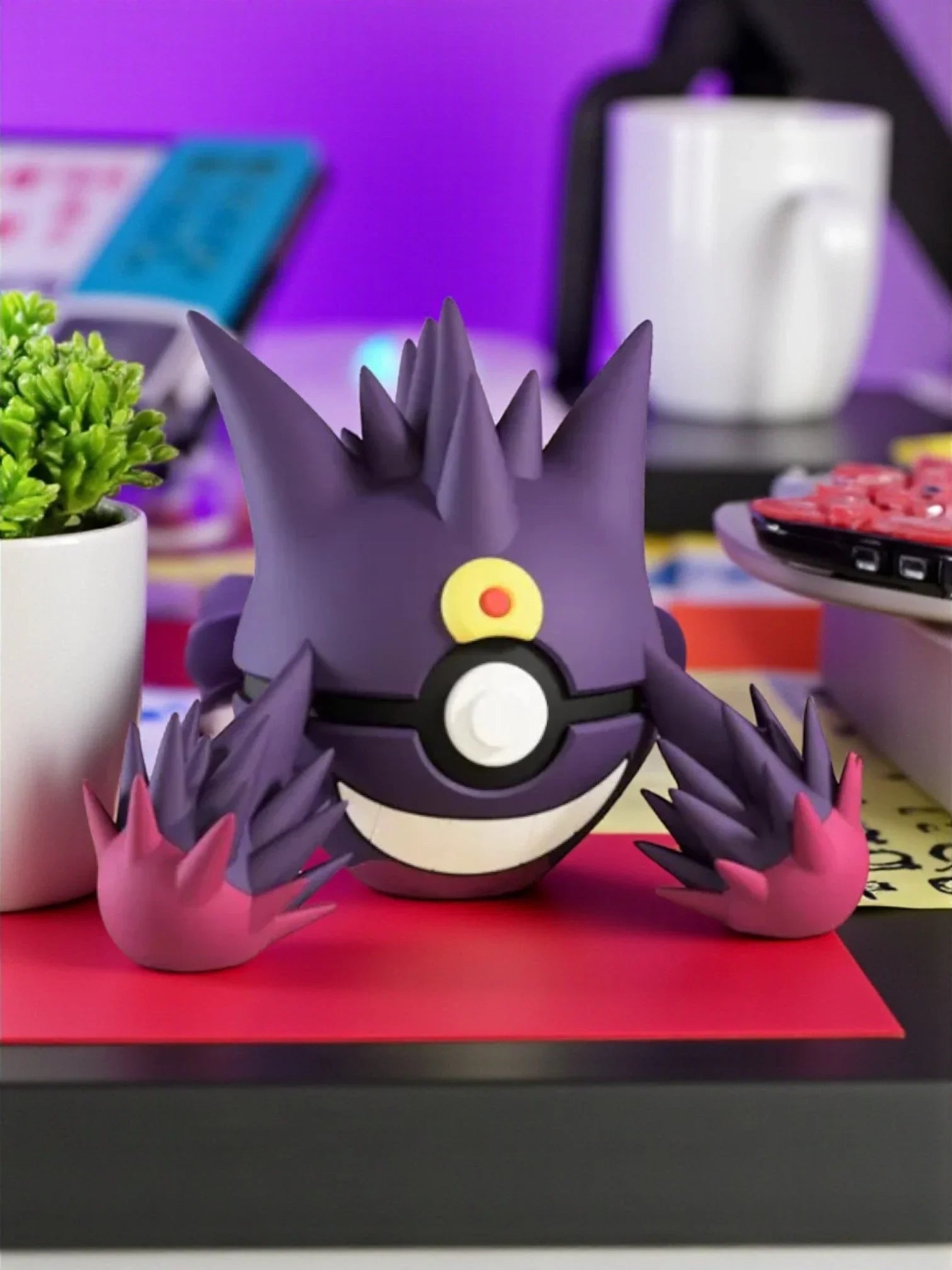 Figura collezionabile Mega Gengar Pokeball su scrivania colorata con tazza e pianta