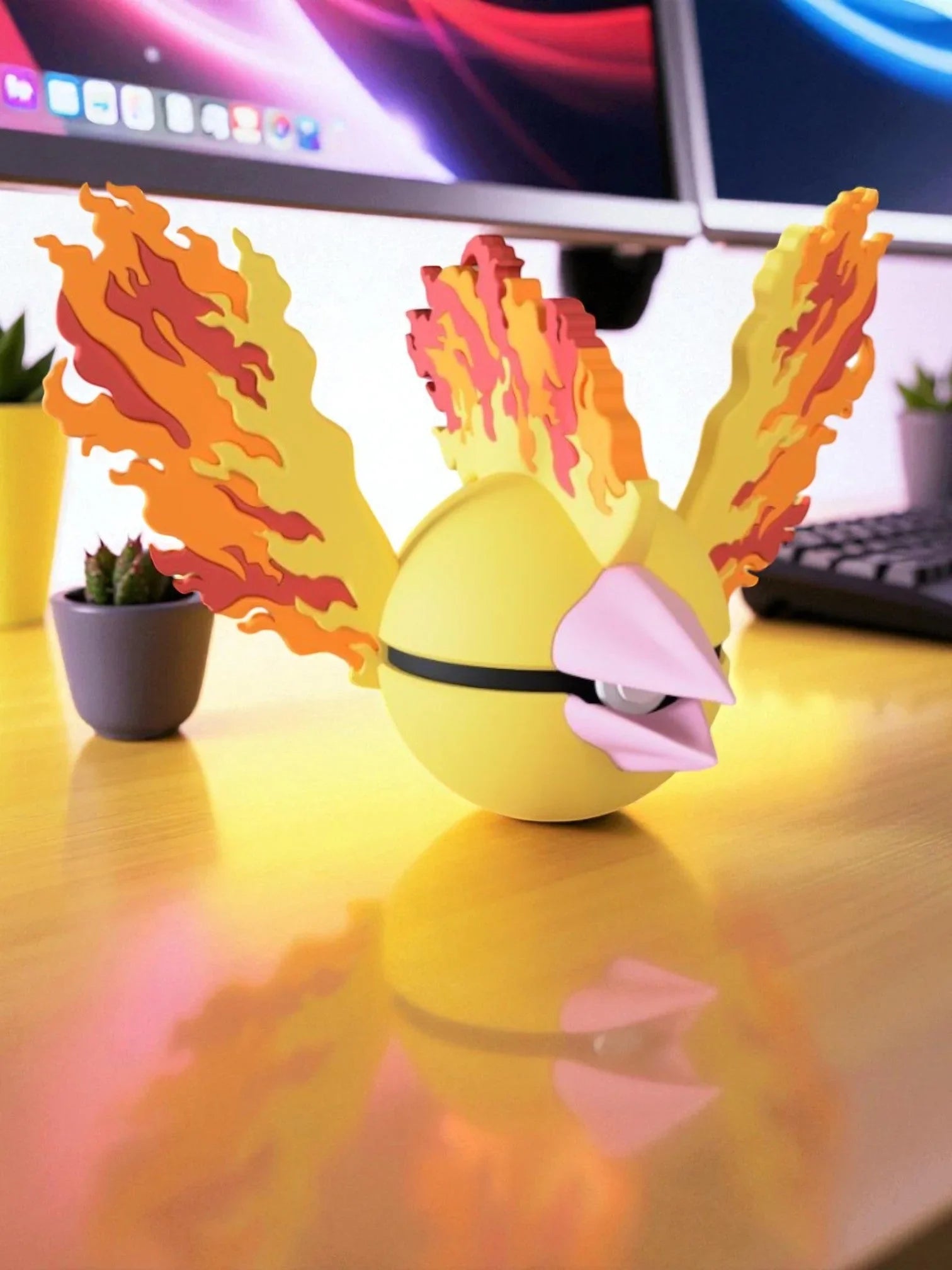 Poké Ball Moltres gialla con ali di fiamme, su scrivania vicino a monitor e tastiera