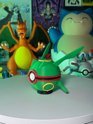 Pokeball Rayquaza verde con base magnetica, esposta su tavolo con sfondo di figure anime e Pokémon.