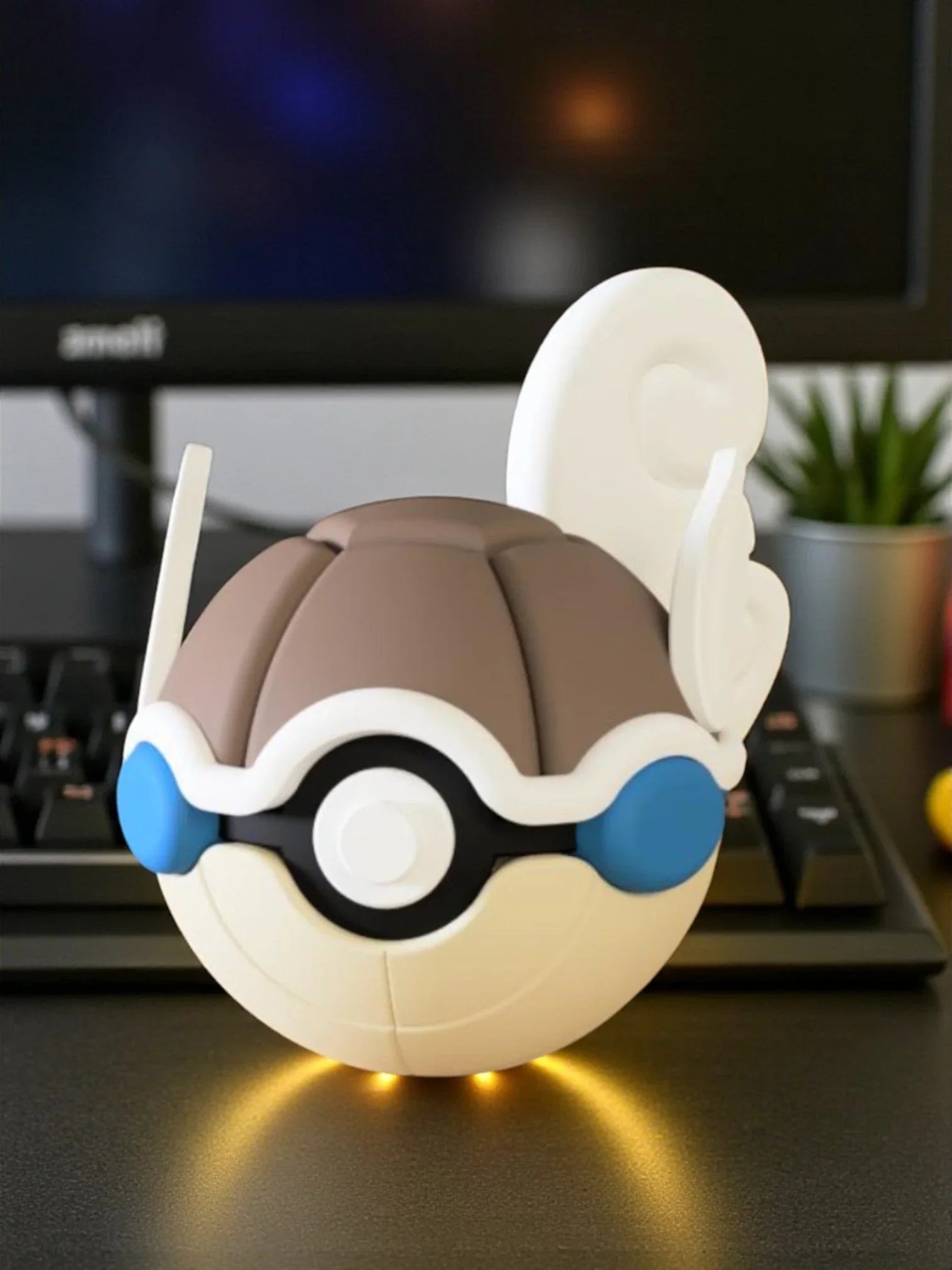 Pokeball ispirata a Wartortle con dettagli blu e coda bianca, su scrivania davanti a tastiera.