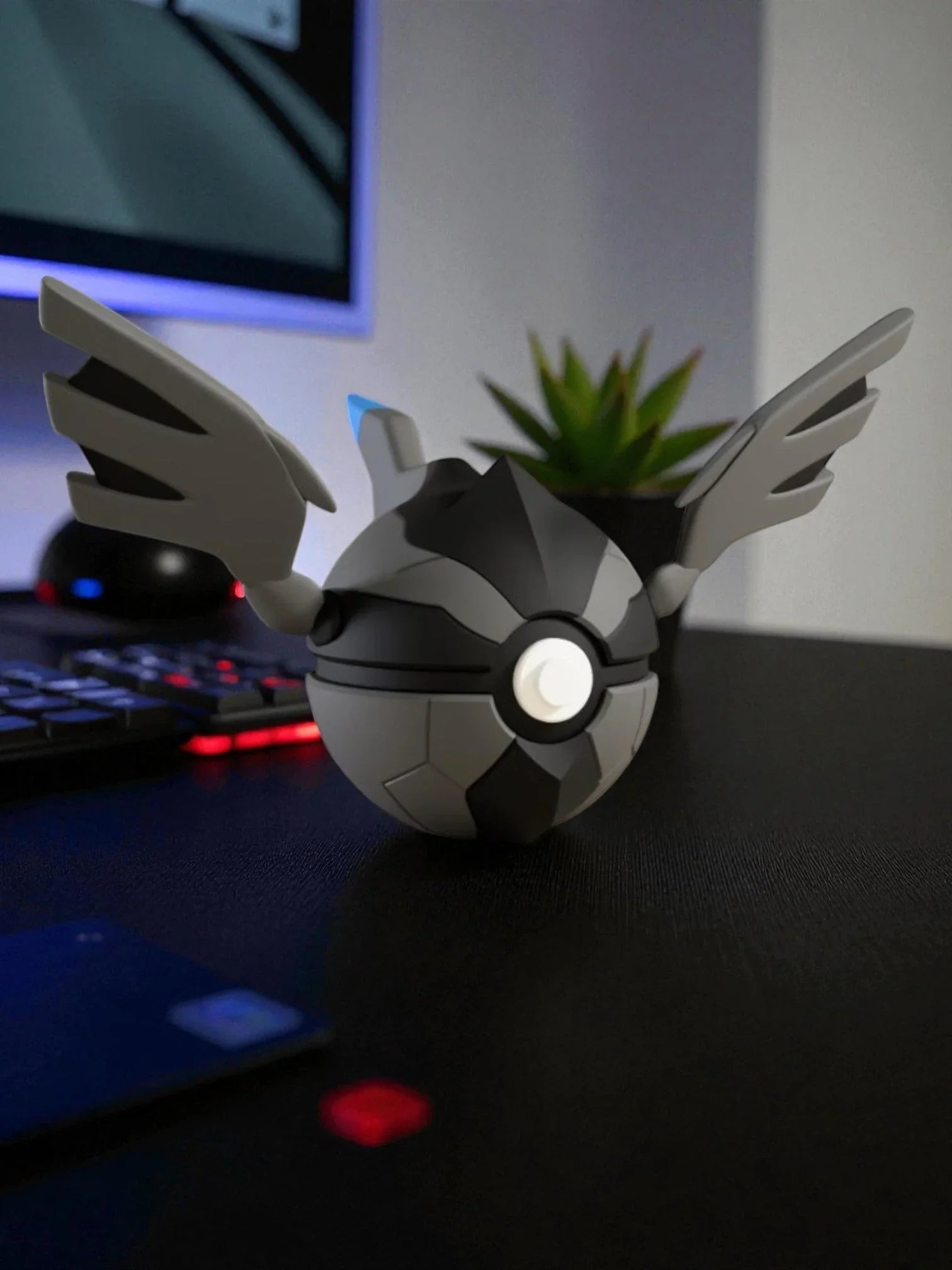 Pokeball Zekrom nera e grigia con ali, esposta su scrivania moderna vicino a tastiera