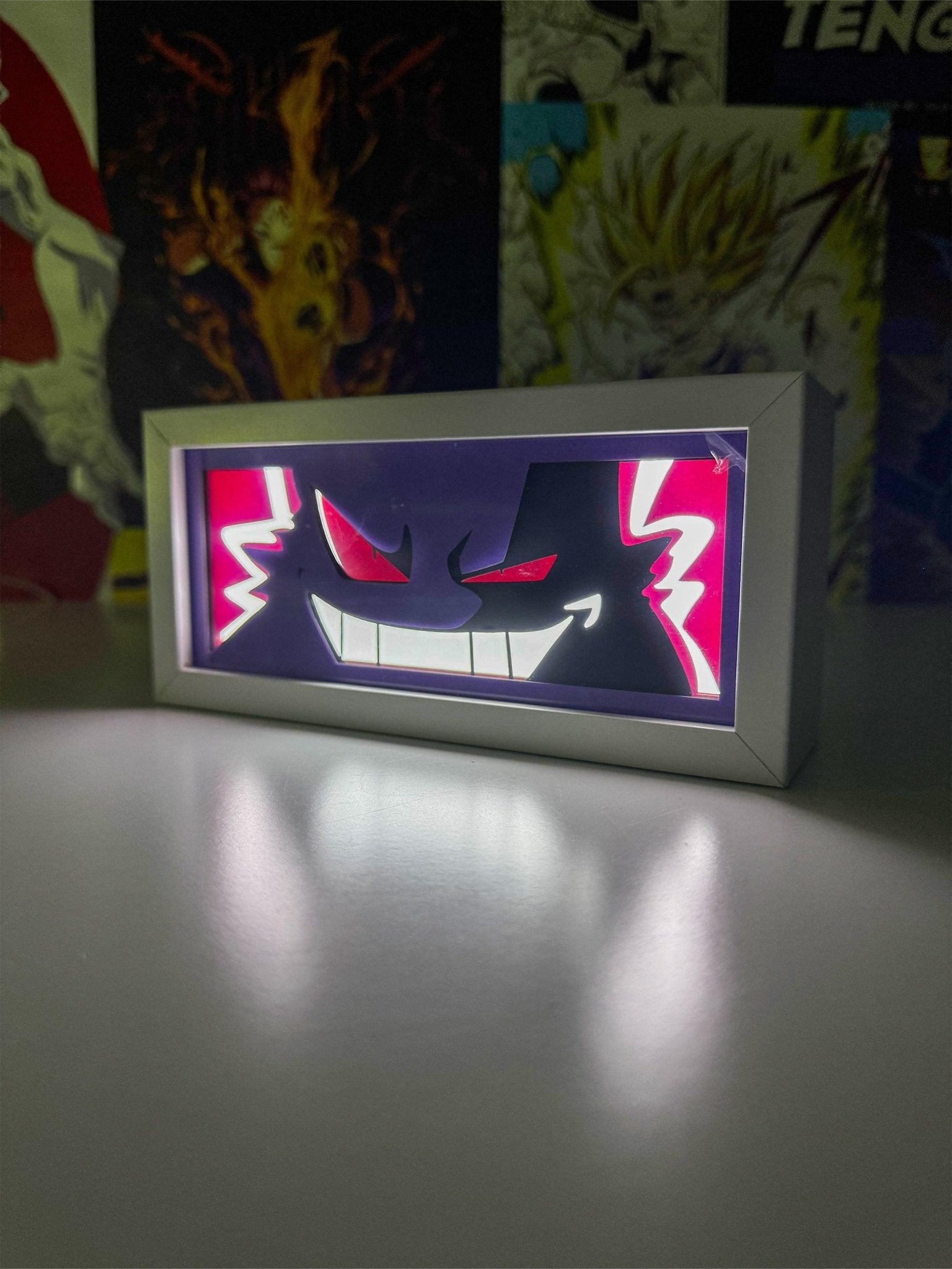 Light box con Gengar di Pokémon illuminato su scrivania, sfondo con poster anime.