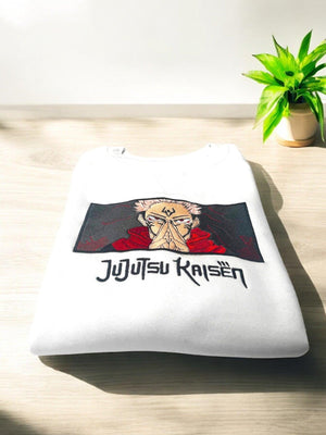 Felpa bianca piegata con ricamo Sukuna di Jujutsu Kaisen, su tavolo chiaro con pianta.
