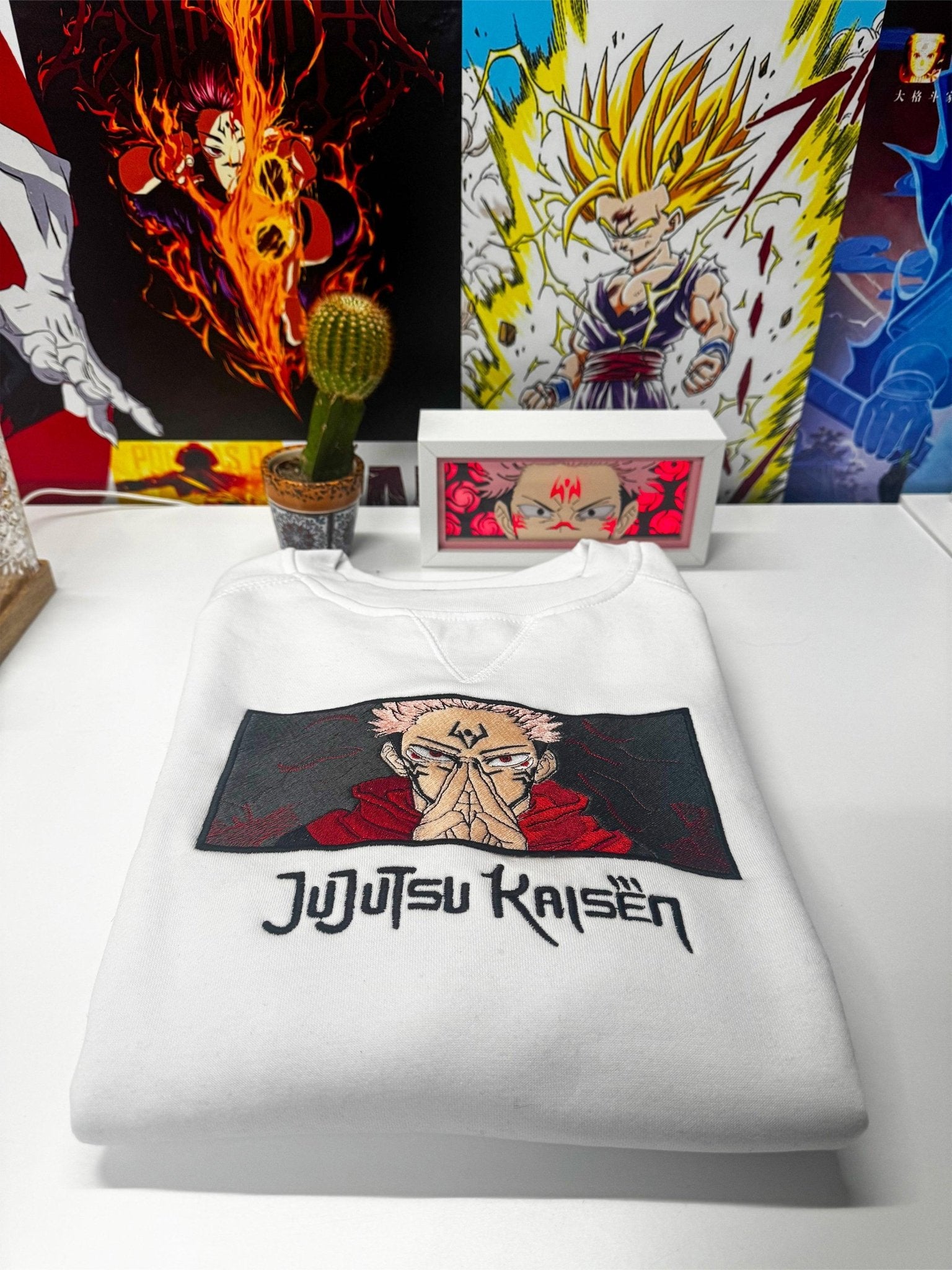 Felpa bianca ricamata Jujutsu Kaisen con Sukuna, ambiente decorato con poster anime.