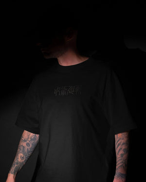 T-shirt nera Jujutsu Kaisen con scritta giapponese ricamata, indossata da uomo tatuato.