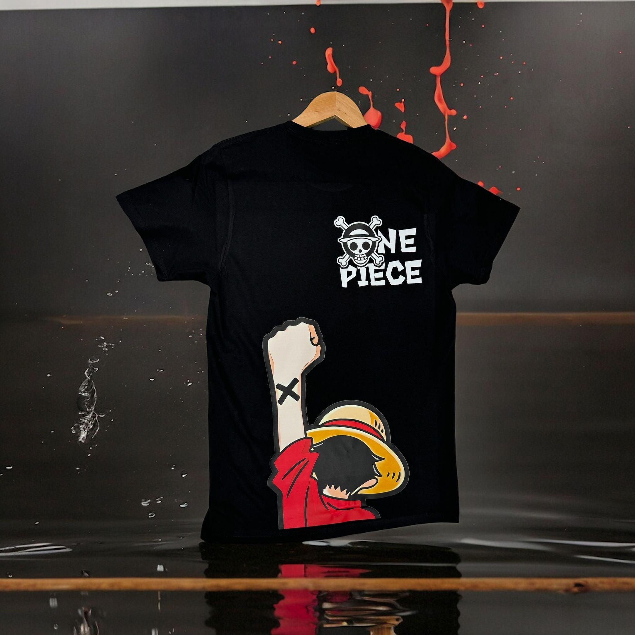 T-shirt nera One Piece con stampa di Luffy e logo Mugiwara, appesa su sfondo scuro.